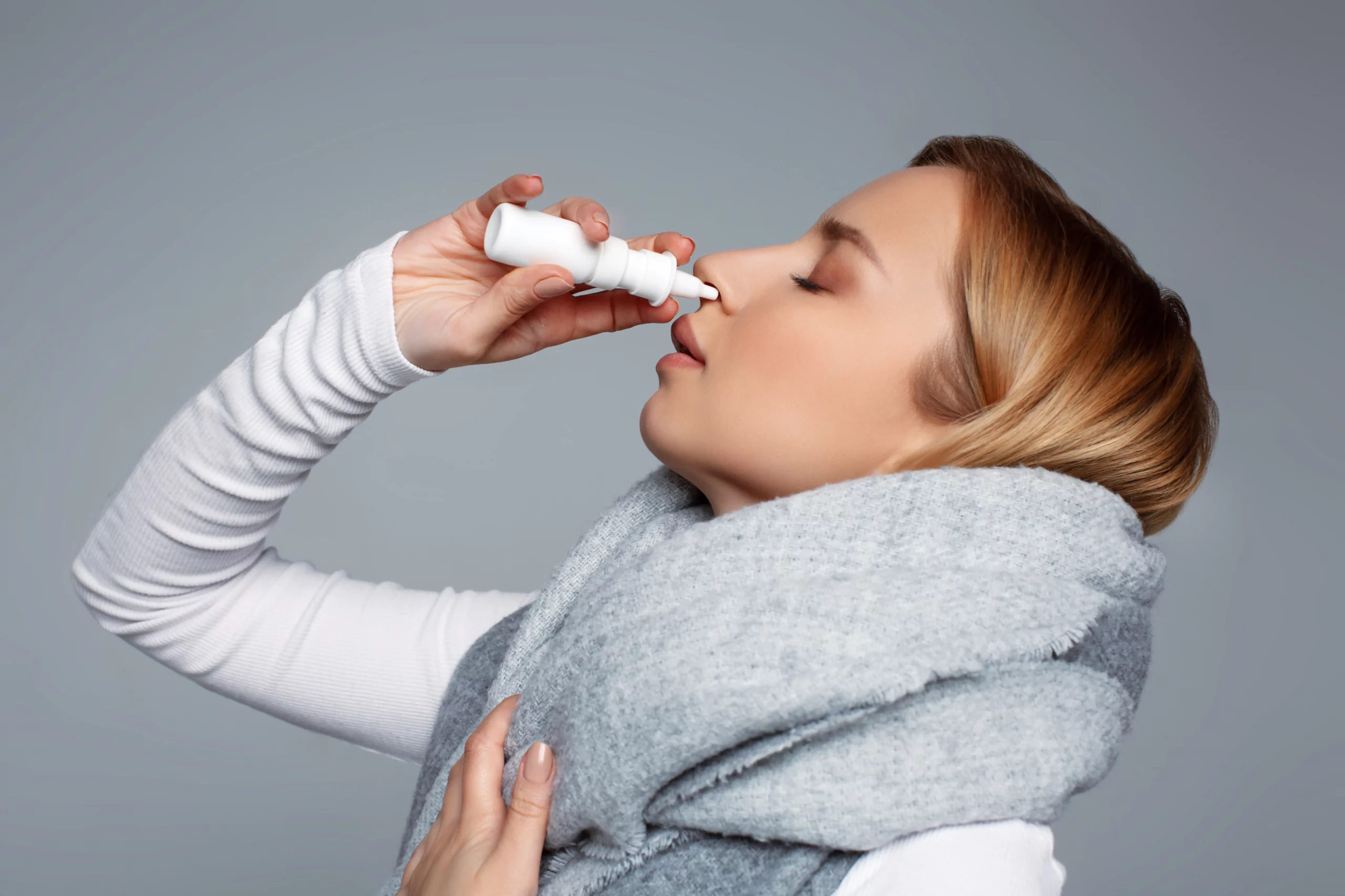 Woman using a nasal spray to relieve allergy or sinus symptoms.
